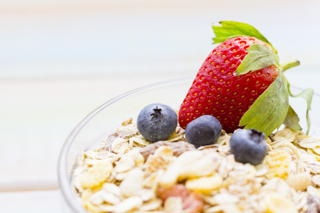 a bowl of oat muesli with candied fruit and fresh strawberry and blueberries in a close up, light...