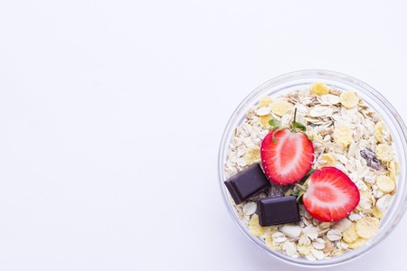Healthy Delicious Breakfast with a bowl of oat muesli with fresh strawberry and pieces of dark chocolate and on white, close up, top viewの写真素材
