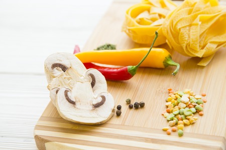 Cooking and Healthy Organic Food concept. Fettuccini, beans, chili peppers and sliced champignon mushrooms on a wooden cutting board, close upの写真素材