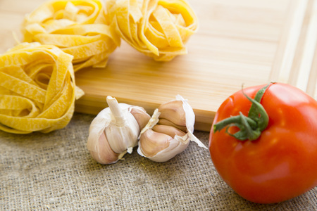 Preparing Food Concept. Ingredients for cooking fettuccini with garlic and tomato on a wooden cutting board, linen textile backgroundの写真素材