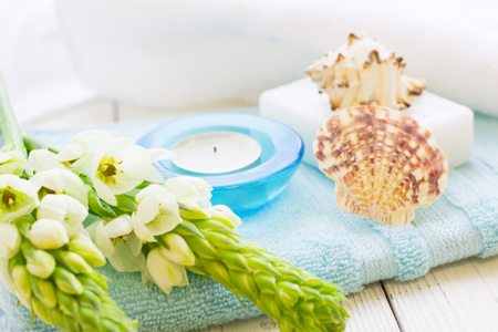 Aromatherapy Spa Concept with a fragrant candle in a blue candle holder, a bar of soap, terry towels, sea shells and white flower on white wooden backgroundの写真素材