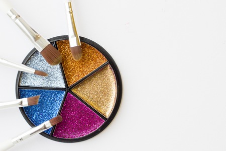 Make Up Beauty Fashion Concept. Glitter palette with set of brushes for bright eye and face make up in a round box on white, top view, flat layの写真素材