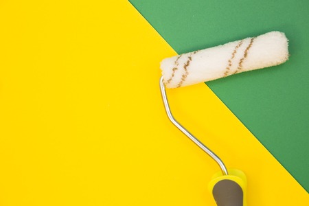 Painting the house. A paint roller on green and yellow background with copy space, top view, flat...