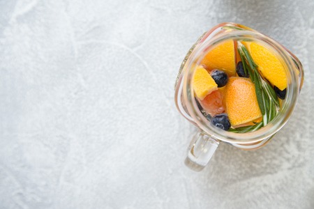 Glass jar of detox water with sliced grapefruit, blueberry and herbs on light concrete background, close upの写真素材