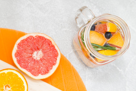 Detox infused water with slices of grapefruit, orange, blueberry and rosemary, halves of orange and grapefruit, light stone and cutting boards as a backgroundの写真素材