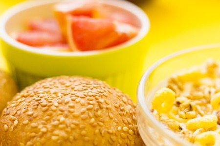 Delicious breakfast: a bowl of muesli, buns and sliced grapefruit on a yellow background with copy space, top viewの写真素材