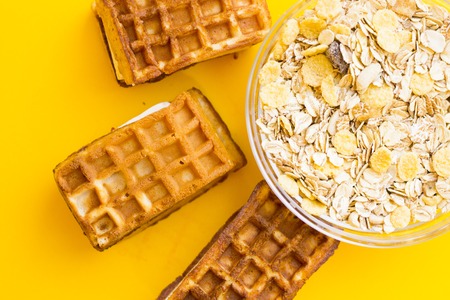 Delicious breakfast: fresh waffles and a bowl of oat flakes on a yellow background with copy space,...