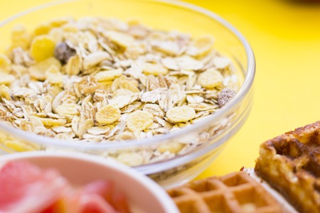 Delicious breakfast: fresh waffles and a bowl of oat flakes grapefruit on a yellow background with...