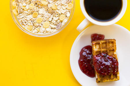 Delicious breakfast: a plate of fresh waffles with raspberry jam, a bowl of cereals and a cup of...