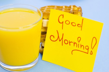 Fresh waffles, a glass of orange juice and Good Morning yellow sticker note on a blue backgroundの写真素材