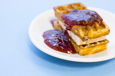 Delicious breakfast: a plate of fresh waffles with raspberry jam on a blue background with copy spaceの写真素材