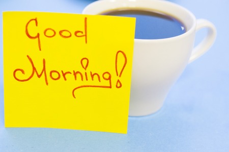 A cup of hot coffee and Good Morning yellow sticker note on a blue backgroundの写真素材
