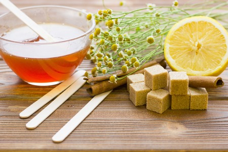 Set of sugaring essentials with natural honey, cinnamon sticks, lemon, camomile and brown sugar on a natural dark wooden backgroundの写真素材