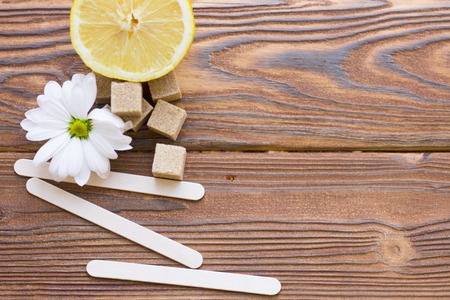 Dark natural wooden background with sugaring essentials: brown sugar cubes, lemon, camomile flower and wooden spatulasの写真素材