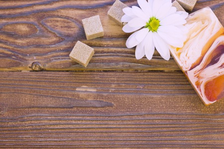 Set of spa essentials with a camomile flower, brown sugar cubes and a bar of soap on a natural dark wooden background, top viewの写真素材