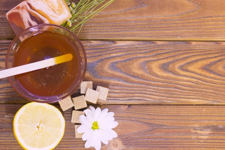 Set of sugaring essentials a bowl of honey, lemon, a bar of fruit soap and brown sugar on a natural dark wooden background, top viewの写真素材