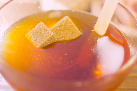 Spa procedures concept. Brown sugar cubes in a bowl of honey, close upの写真素材