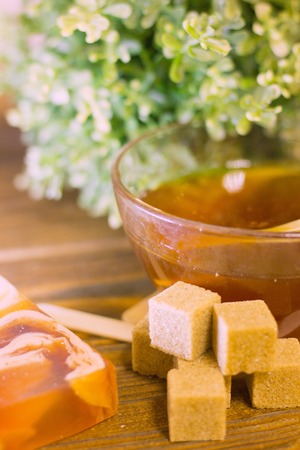 A set of spa essentials with a bowl of honey, fruit soap, lemon brown sugar and a green plant on a natural dark wooden background, close upの写真素材
