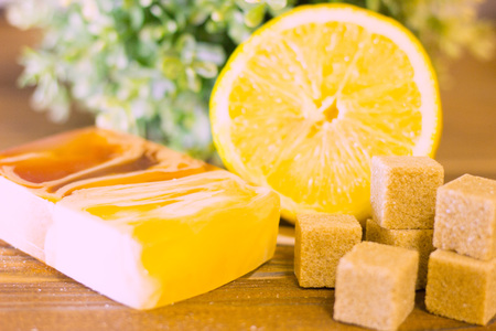 A set of spa essentials with fruit soap, lemon, brown sugar and a green plant on a natural dark...