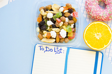 Planning a day. A container of candy fruit, an orange, strawberry donut and a notebook with To Do List inscription, top view, blue and white squared paper backgroundの写真素材