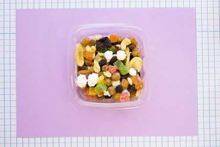 A container of candy fruit, top view, lilac and white squared paper background