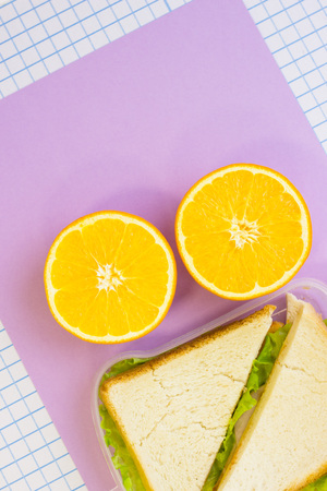 Orange cut in half and a fresh sandwich in a box , top view, lilac and white squared paper backgroundの写真素材