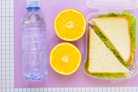Orange cut in half, a bottle of water and a fresh sandwich in a box , top view, lilac and white squared paper backgroundの写真素材