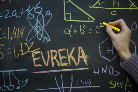 Eureka inscription, graphs and formulas on a black chalkboard, a woman's hand writing with a yellow chalkの写真素材