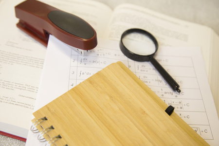 Math tasks and formulas, magnifying glass and stapler on a white tableの写真素材