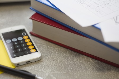 Books, formulas and a phone with calculator on a light stone background, close upの写真素材