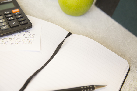 An opened notebook, an apple and calculator on a white tableの写真素材