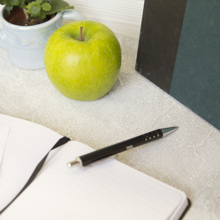 An opened notebook, an apple, a calculator and plant in a pot on a white table, close upの写真素材