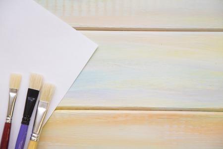Brushes and a sheet of paper on colored wooden background with copy space, close up, top viewの写真素材