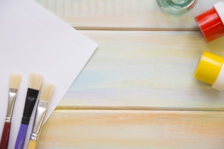 Brushes, gouache paint and a sheet of paper on colored wooden background with copy space, close up, top viewの写真素材