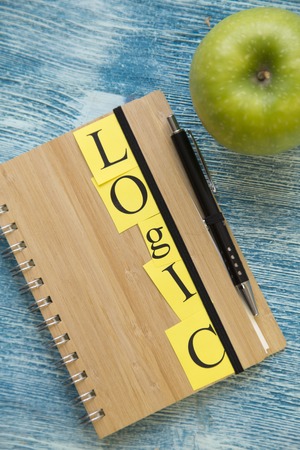 School supplies: a wooden notebook with Logic inscription and a green apple on a blue wooden background, top view, copy spaceの写真素材