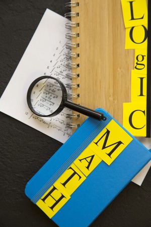 Math inscription on a blue notebook, Logic inscription on a wooden notebook, magnifying glass and paper with formulas, black stone background, top viewの写真素材