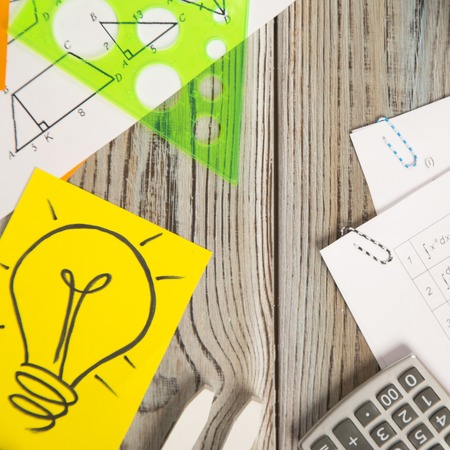 Papers with formulas, calculator and a light bulb image on a grey wooden background, top view, copy spaceの写真素材