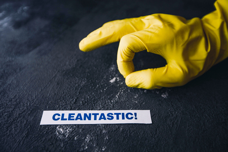 Cleaning office or house concept. Mens hand in yellow rubber glove pointing to Cleantastic inscription sign, concrete dark background, top view, copy spaceの写真素材