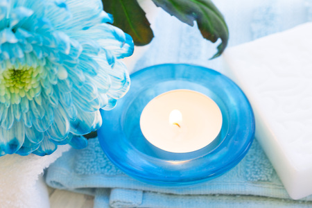 Spa items set with a blue flower, towels, a bar of soap and a candle in blue glass holder, close up, white backgroundの写真素材