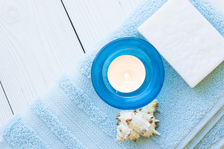 Spa items set with a bar of soap, sea shells and a burning candle on a blue towel, close up, white background, top viewの写真素材
