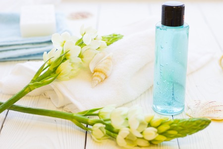 Spa items set with a blue bottle of showel gel, sea shells, flower spur and clean towels, white wooden backgroundの写真素材