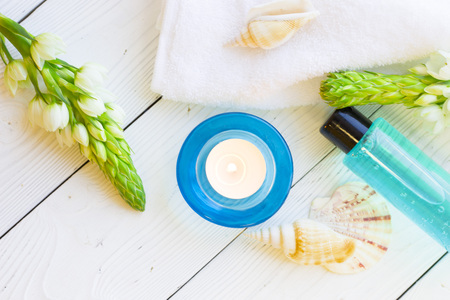 Spa items set with a blue bottle of showel gel, sea shells, flower spur,a burning candle and clean towels, white wooden background, top view, flat layの写真素材