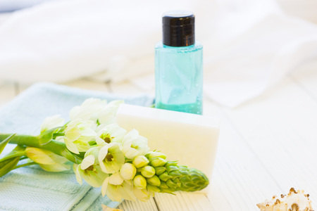 Spa items set with a white flower spur on a blue towel, a bar of soap and a bottle of showel gel, white wooden background, close upの写真素材