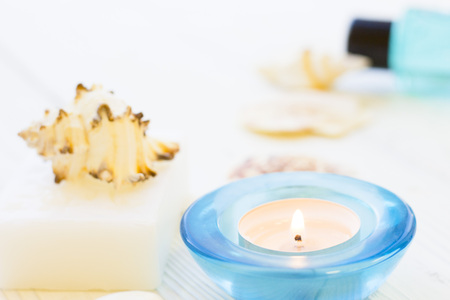 Spa items set with a bar of soap, sea shells and a burning candle in a blue holder , white wooden background, close upの写真素材