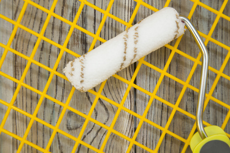 A paint roller on a yellow grid, grey wooden background with copy space, top view, close up