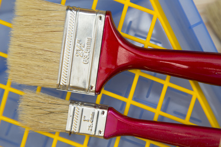 Red wooden paint brushes on a blue plastic pan and a yellow grid, top view, close up