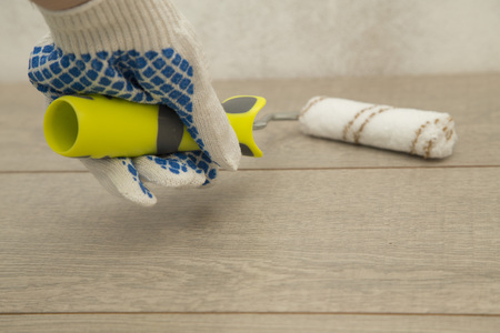 Man's hand in protective glove is painting a light wooden plank with a paint roller, close up, top viewの写真素材