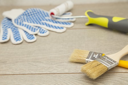 Repair, Redecorating Concept. Paint brushes, roller and a pair of protective work gloves on a light wooden background, close upの写真素材