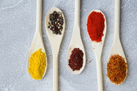 Dry spices and herbs in wooden spoons on a light stone background with copy space, top view, flat layの写真素材