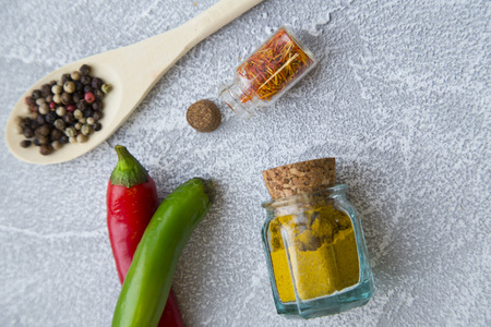 Dry spices and herbs in wooden spoons and glass jars with fresh chili peppers on a light stone background with copy space, top view, flat layの写真素材
